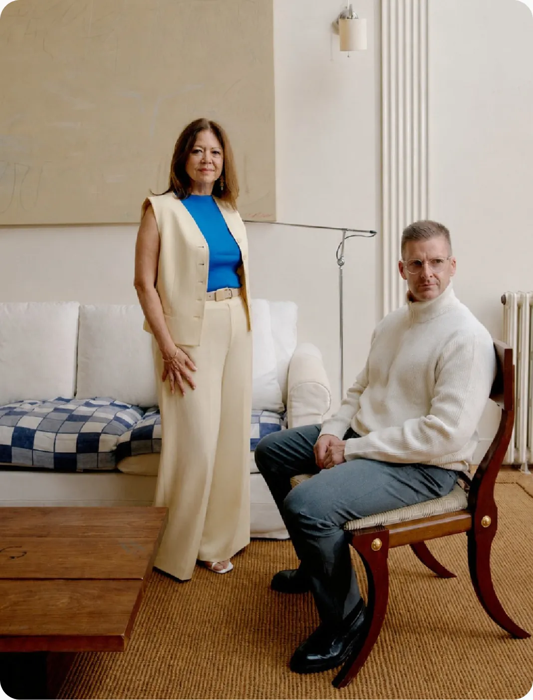 Two members of the Pure Bold team in a living room, one standing beside a sofa and one seated on a wooden chair