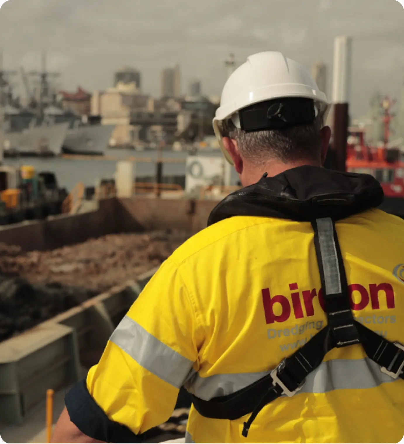 Worker in a yellow Birdon hi-vis vest and hard hat at a port