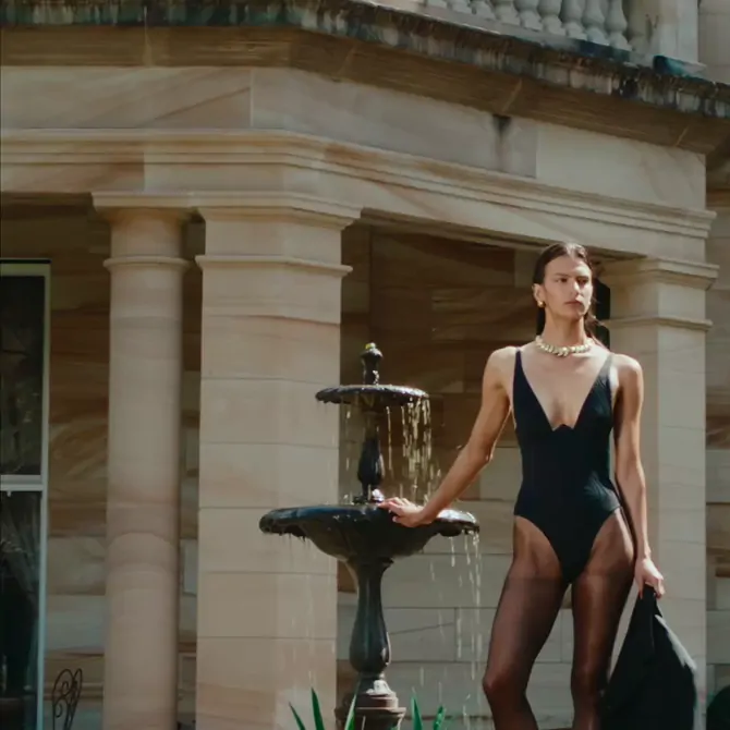 Model in a black swimsuit beside a stone fountain